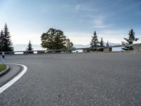 the parking lot for the motorcyclist is empty near trees and buildings, but it has no roads