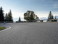 the parking lot for the motorcyclist is empty near trees and buildings, but it has no roads