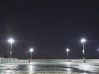 an empty parking lot full of street lights at night time with the ground wet and the roadway reflecting off