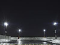 an empty parking lot full of street lights at night time with the ground wet and the roadway reflecting off