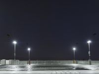 an empty parking lot full of street lights at night time with the ground wet and the roadway reflecting off
