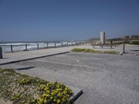 an empty parking lot next to the ocean with several flowers in front of it and a bench overlooking the ocean