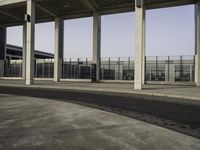 there is an empty parking lot with an open building behind it and cars in the distance