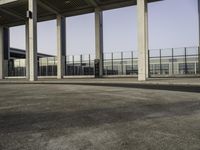 there is an empty parking lot with an open building behind it and cars in the distance