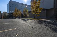 this is an empty parking lot with trees in front of a building and one street