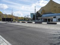 the parking lot is empty outside of the modern building and next to the street lined with stone benches