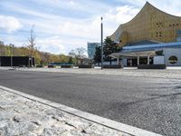 the parking lot is empty outside of the modern building and next to the street lined with stone benches