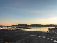 empty parking lot in front of small pier with houses in the background at sunset time