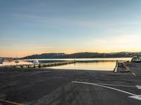 empty parking lot in front of small pier with houses in the background at sunset time