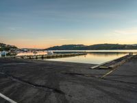 empty parking lot in front of small pier with houses in the background at sunset time