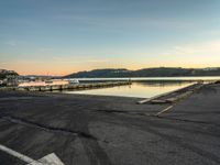 empty parking lot in front of small pier with houses in the background at sunset time