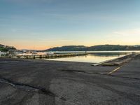 empty parking lot in front of small pier with houses in the background at sunset time