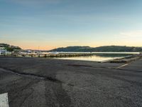 empty parking lot in front of small pier with houses in the background at sunset time