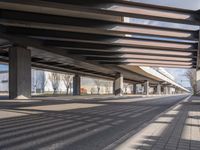 a empty parking lot next to a rail line of metal structures and brick floors with large shadows