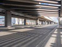 a empty parking lot next to a rail line of metal structures and brick floors with large shadows