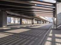 a empty parking lot next to a rail line of metal structures and brick floors with large shadows