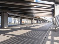 a empty parking lot next to a rail line of metal structures and brick floors with large shadows