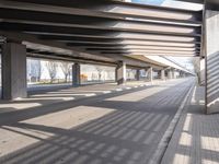 a empty parking lot next to a rail line of metal structures and brick floors with large shadows