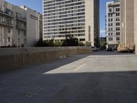 an empty parking lot in front of some building next to tall buildings and street with cars