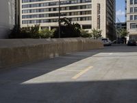 an empty parking lot in front of some building next to tall buildings and street with cars