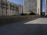 an empty parking lot in front of some building next to tall buildings and street with cars