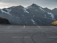 an empty parking lot with snow capped mountains in the background with a road marked with circles