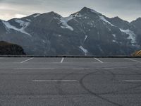 an empty parking lot with snow capped mountains in the background with a road marked with circles