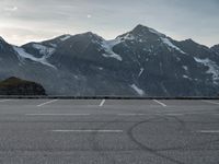 an empty parking lot with snow capped mountains in the background with a road marked with circles