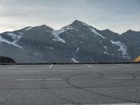 an empty parking lot with snow capped mountains in the background with a road marked with circles