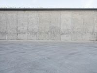 an empty parking lot and street with a big cement wall in the background and another building and street light