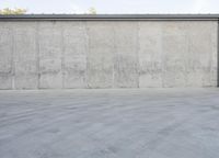 an empty parking lot and street with a big cement wall in the background and another building and street light