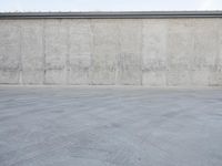 an empty parking lot and street with a big cement wall in the background and another building and street light