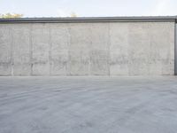 an empty parking lot and street with a big cement wall in the background and another building and street light