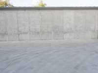 an empty parking lot and street with a big cement wall in the background and another building and street light