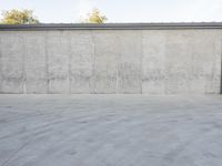 an empty parking lot and street with a big cement wall in the background and another building and street light