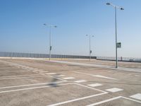 empty parking lot and street lamps along a sidewalk with blue skies above it's surface