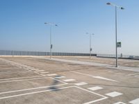 empty parking lot and street lamps along a sidewalk with blue skies above it's surface