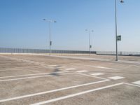 empty parking lot and street lamps along a sidewalk with blue skies above it's surface