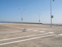 empty parking lot and street lamps along a sidewalk with blue skies above it's surface