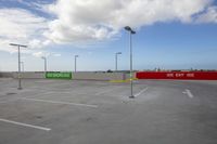 an empty parking lot with a large red sign near street lamps and a blue sky background