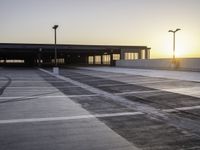 an empty parking lot at sunrise with sun reflecting off the building's windows and lighting poles