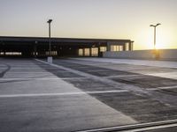 an empty parking lot at sunrise with sun reflecting off the building's windows and lighting poles