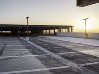 an empty parking lot at sunrise with sun reflecting off the building's windows and lighting poles