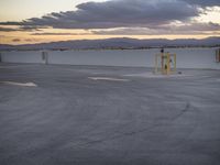 an empty parking lot with the sun setting in the background by the water in front