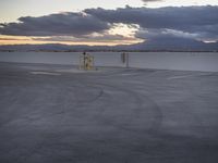 an empty parking lot with the sun setting in the background by the water in front