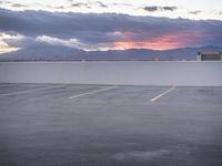 an empty parking lot with the sun setting in the background by the water in front