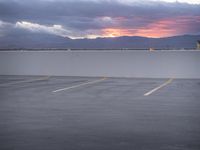 an empty parking lot with the sun setting in the background by the water in front