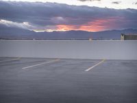 an empty parking lot with the sun setting in the background by the water in front