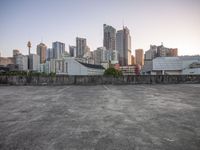 an empty parking lot with a tall city in the background and skyscrapers behind it