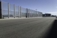 empty parking lot on a clear day with fencing and a car parked next to it